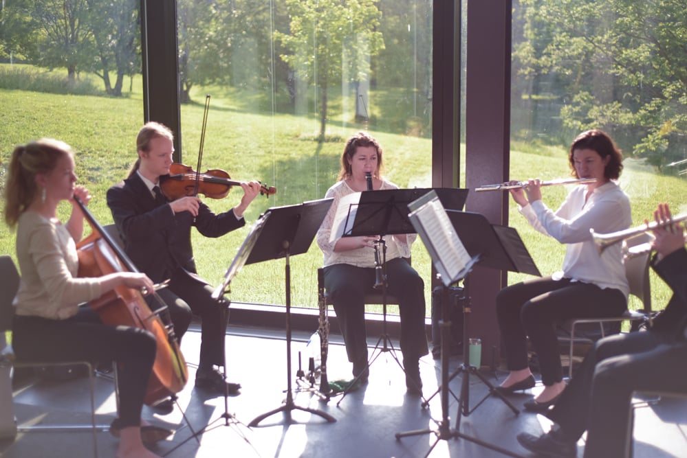 Musicians play stringed and brass instruments in the sunlit atrium.