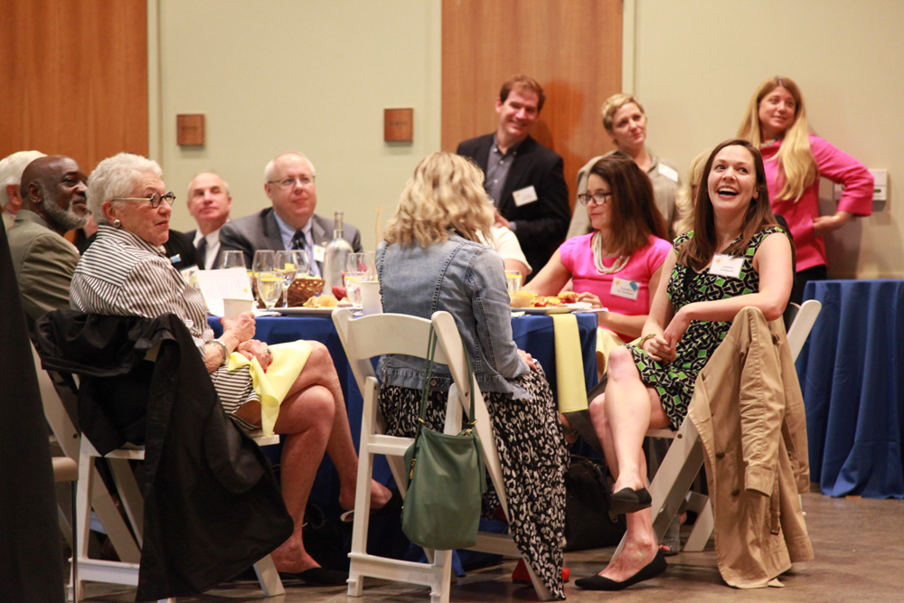 Guests smiling and laughing as they gathered around tables set with a delicious breakfast of fruit, juice, biscuits, and candied bacon.