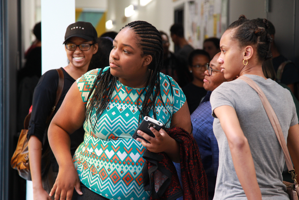 Interns are gathered in a hallway. A teenage girl in the foreground is glancing to her right. Another girl in a baseball cap smiles brightly behind her.