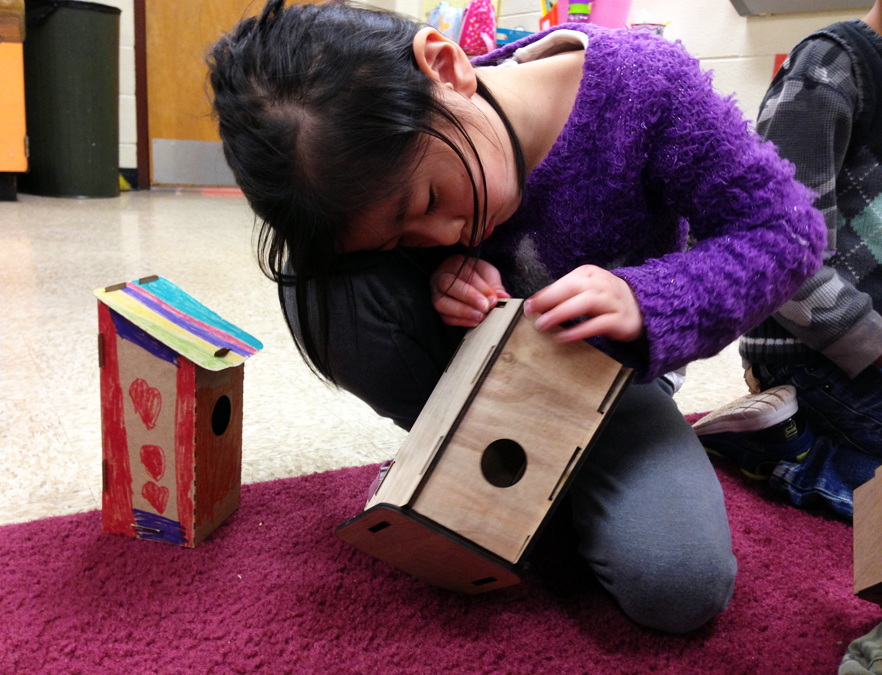 A child assembling a laser-cut, wooden birdhouse