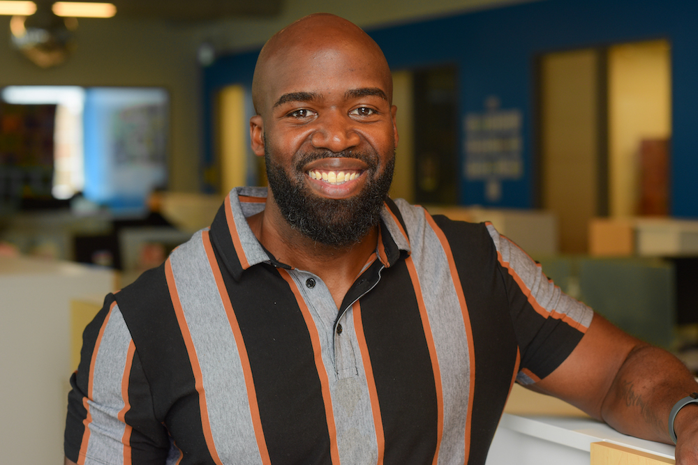 A close-up photograph of DJ Brooks standing in the office space