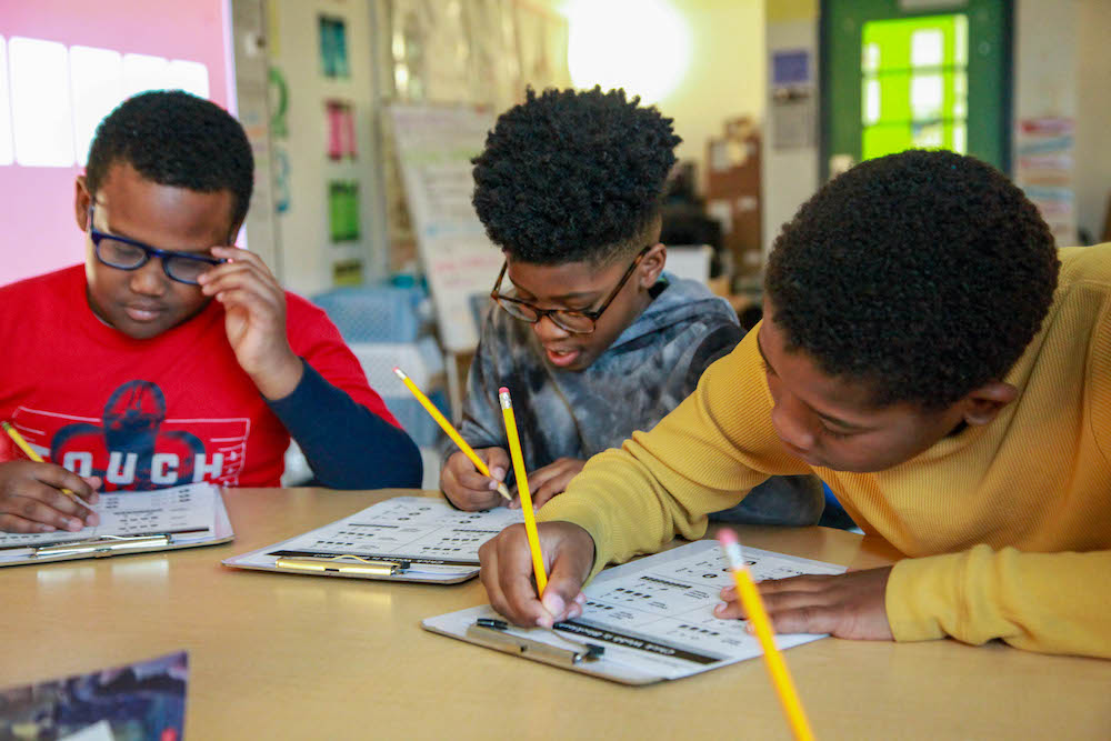 Three students completing a worksheet with pencils.