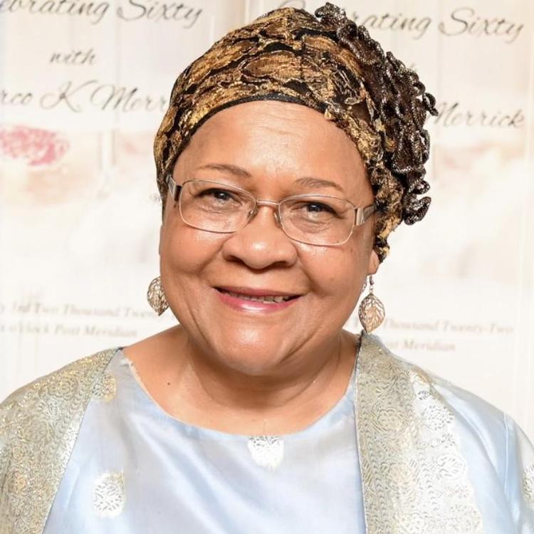 head shot of a woman dressed in neutrals smiling, wearing glasses, earrings, and a fabric headband.