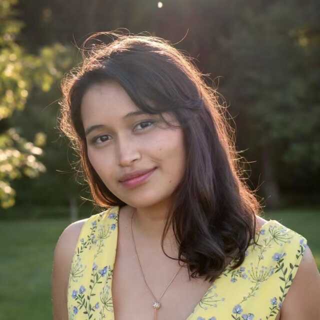 Woman smiling into the camera in soft sunlight wearing a yellow dress.